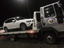 Reboque transportando um carro branco em uma plataforma à noite.