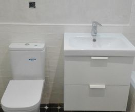 Baño moderno con inodoro blanco, lavabo cuadrado y azulejos negros en el suelo.