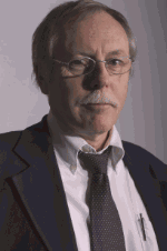 Älterer Mann im Anzug mit Krawatte und Brille, schaut ernst in die Kamera.