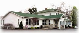White building with green roof, surrounded by trees and shrubs, featuring a wheelchair ramp.