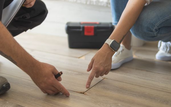 Hausbesitzer und Gutachter begutachten wassergeschädigtes, aufgequollenes Laminat.