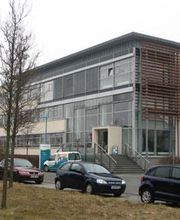 Modernes Bürogebäude mit Glasfassade und geparkten Autos davor.