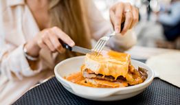 Een persoon snijdt een belegd broodje met smeltende kaas op een bord.