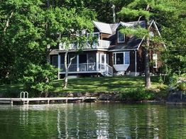 House by a lake surrounded by trees, with a small dock extending into the water.