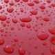 Water droplets on a glossy red surface, varying in size and reflecting light.