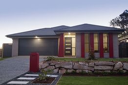 Modern suburban house with red and gray accents, large windows, and a stone-lined front yard.