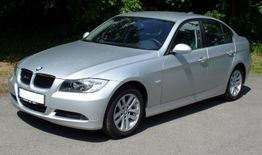 Silberner BMW 3er auf einer Straße, umgeben von grünen Bäumen im Hintergrund.