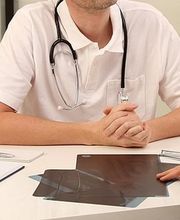 Arztgespräch: Eine Person spricht mit einem Arzt am Schreibtisch, Röntgenbilder sind darauf.