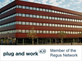 Moderne Bürogebäude mit roter Fassade, darunter "plug and work" und "Member of the Regus Network".