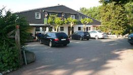 Parkplatz vor einem Gebäude mit mehreren Autos und Bäumen im Hintergrund.