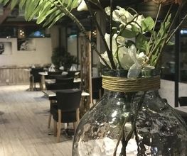 Vase mit weißen Blumen in einem stilvollen Restaurant mit Holztischen und Stühlen im Hintergrund.