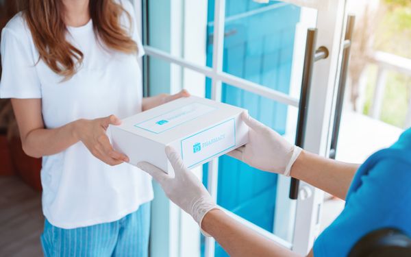 Eine kranke Frau nimmt zu Hause eine Online-Bestellung aus der Apotheke entgegen.