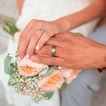 Ein frisch verheiratetes Ehepaar hält die Hände über einem Blumenstrauß zusammen, um die Eheringe zu fotografieren.