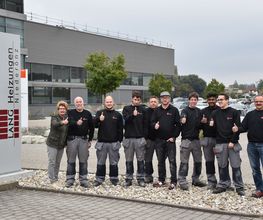 Personengruppe vor Gebäude der Firma „Lang Heizungen“, Daumen hoch.