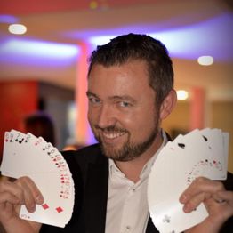 Un homme souriant montre deux éventails de cartes dans un cadre lumineux.