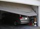 Car stuck under a partially closed garage door in a cluttered garage.