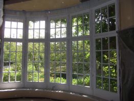 Großes Erkerfenster mit Blick auf grüne Bäume und Sonnenschein.