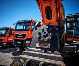 Baumaschinen und LKWs auf einem Betriebshof bei sonnigem Wetter.