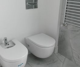 Baño moderno con bidé y váter de diseño minimalista en una pared blanca.
