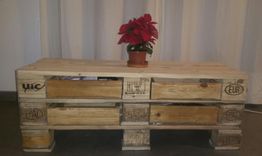 Mesa de palés con maceta de poinsettia roja encima, cortina blanca de fondo.