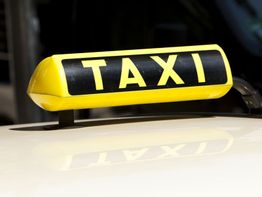 Gelbes Taxischild auf einem Auto bei Tageslicht, mit schwarzem Hintergrund.