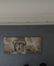 Parete soggiorno grigia con dipinto di Buddha, decorazioni floreali viola e luce soffusa.