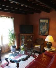 Sala de estar rústica con sofá rojo, mesa de cristal, plantas y lámpara de mesa junto a ventana.