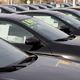 Row of black cars with price stickers on windshields parked at a dealership.