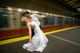 Bride and groom kiss on a subway platform as a train passes by.