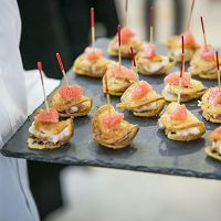 Tray of bite-sized appetizers with toothpicks, topped with pink garnish, served by a waiter.