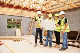 Construction workers in helmets review blueprints inside a building under construction.