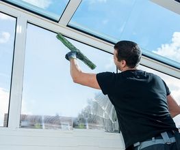 Mann reinigt große Glasfenster mit Blick auf den blauen Himmel.