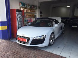 Auto deportivo blanco estacionado en un taller con estantería de aceites y una máquina expendedora.