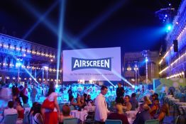 Freiluftkino bei Nacht mit vielen Menschen und einem großen AIRSCREEN-Display auf einem Platz.