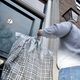 Persoon hangt kleding in een hoes aan deur nummer 9 in een stadsomgeving.