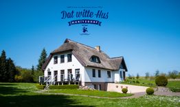 Reetgedecktes Haus auf grüner Wiese, blauer Himmel, Schriftzug "Dat witte Hus Moritzdorf".
