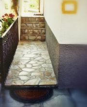 Steinweg mit Blumen auf der linken Seite; führt zu einer Haustür mit Stufen.