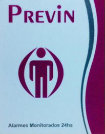 Placa com o texto "PREVIN" e "Alarmes Monitorados 24hs" com ícone de pessoa estilizada.
