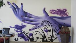 Wandbild mit lila Händen und floralen Mustern, links ein Stuhl und weiße Wand mit Kunst.