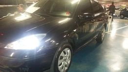 Carro preto estacionado em uma garagem, visto de frente, com os faróis acesos.