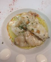 Plato de pescado en salsa con hierbas y piñones, decorado con gotas de crema en el borde.