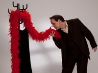 Mann im Anzug neigt sich zu roter Federboa an Garderobenständer.