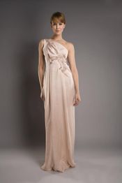 Frau in einem eleganten, cremefarbenen Schulterkleid, stehend vor grauem Hintergrund.