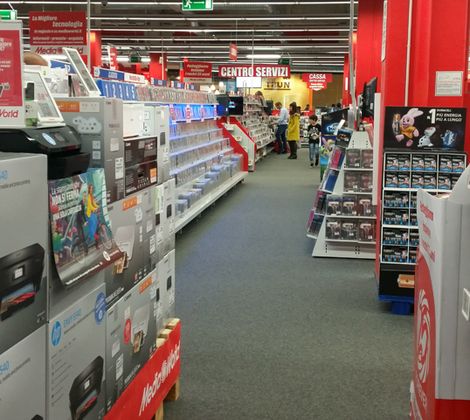 Negozio di elettronica con scaffali pieni di stampanti HP e accessori. Personale sullo sfondo.
