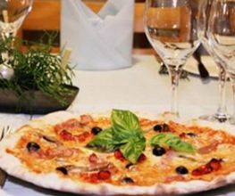 Pizza auf gedecktem Tisch mit Weingläsern und Besteck, dekoriert mit Basilikumblättern.