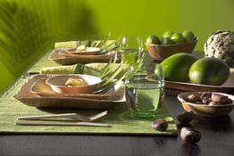 Grün gedeckter Tisch mit Geschirr, Gläsern, Limonen, Mangos und Artischocke.