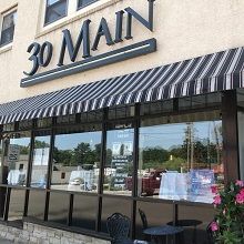 Storefront of "30 Main" with a striped awning and outdoor seating.
