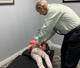 Man adjusting child's back on a chiropractic table in a clinic room.