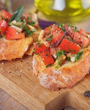 Bruschetta con pomodori freschi, cipolla e erbe su tagliere di legno.