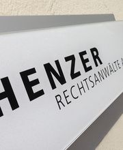 Hinweisschild an einer Wand mit der Aufschrift "HENZER RECHTSANWÄLTE AG".